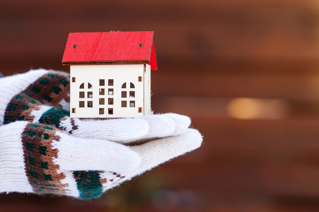 Gloved hands holding a house model in winter